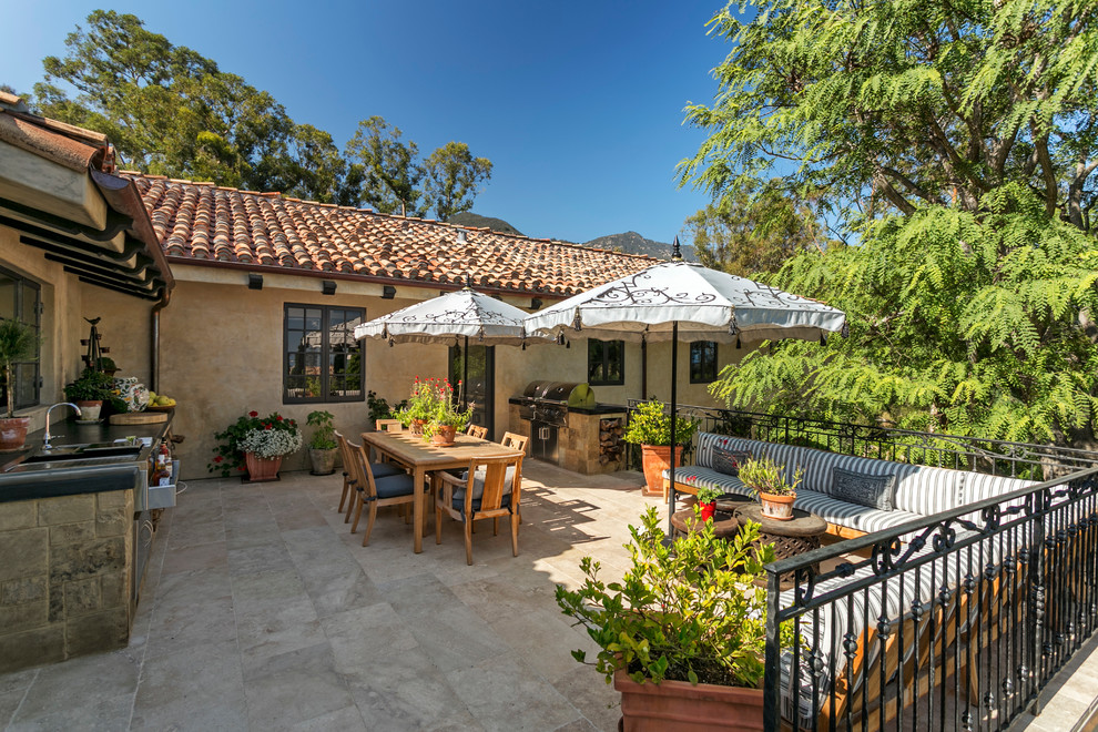 This is an example of a large mediterranean back patio in Santa Barbara with an outdoor kitchen, natural stone paving and no cover.