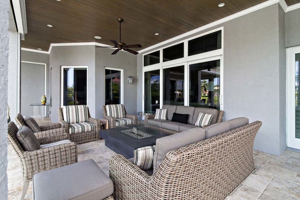 Photo of a large contemporary back patio in Miami with a fire feature, natural stone paving and a roof extension.
