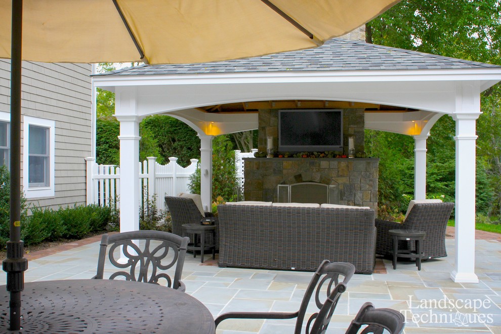 Réalisation d'une grande terrasse arrière champêtre avec un foyer extérieur, des pavés en pierre naturelle et un gazebo ou pavillon.