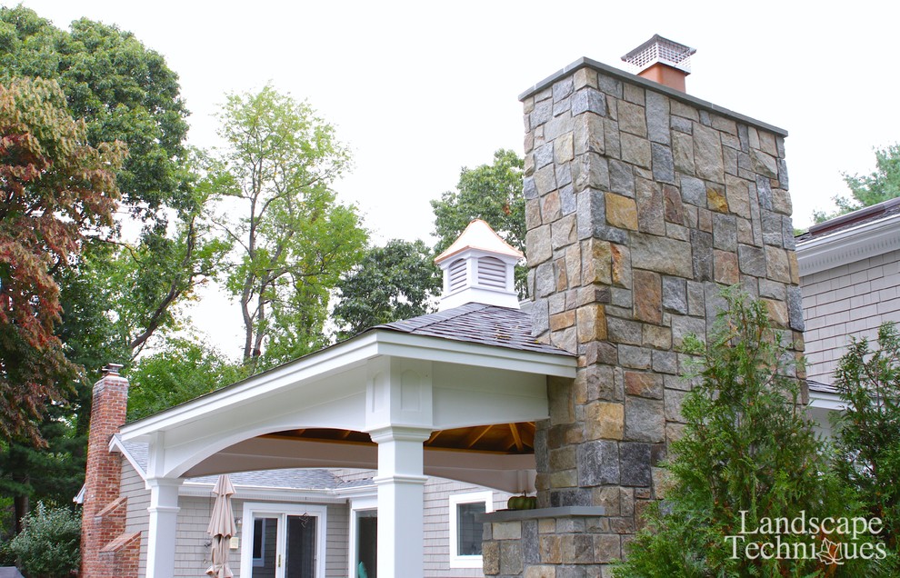 This is an example of a large farmhouse back patio in New York with a fire feature, natural stone paving and a gazebo.