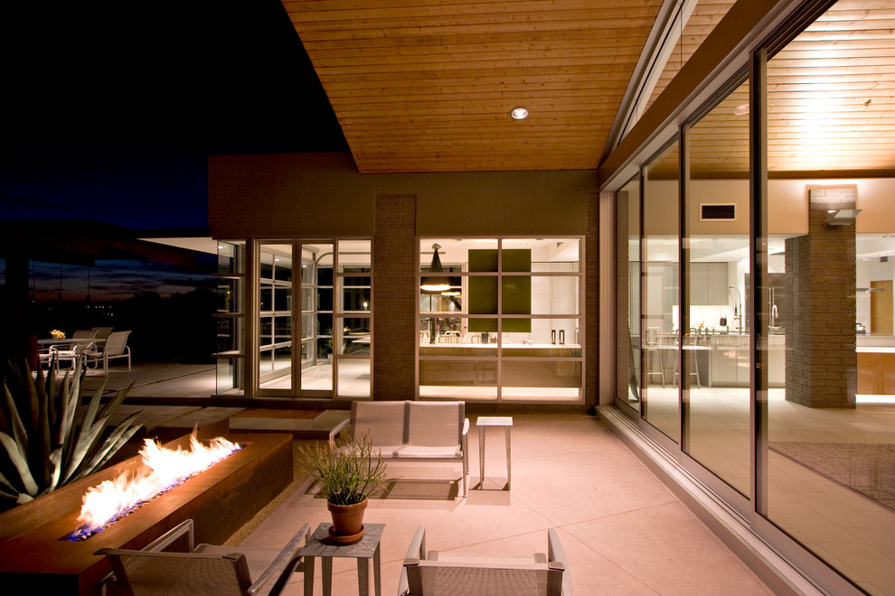 Cette photo montre une terrasse moderne avec un foyer extérieur et une extension de toiture.