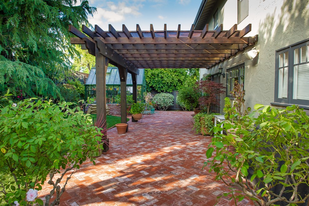 Ejemplo de patio clásico de tamaño medio en patio trasero con jardín de macetas, adoquines de ladrillo y pérgola