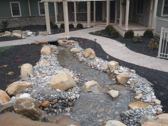Photo of an expansive classic side patio in Philadelphia with a water feature, concrete paving and an awning.