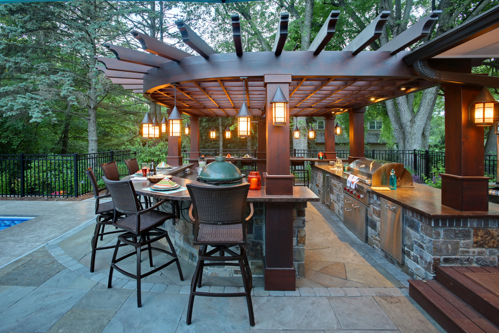 Cette photo montre une terrasse arrière chic avec une cuisine d'été, des pavés en pierre naturelle et une pergola.