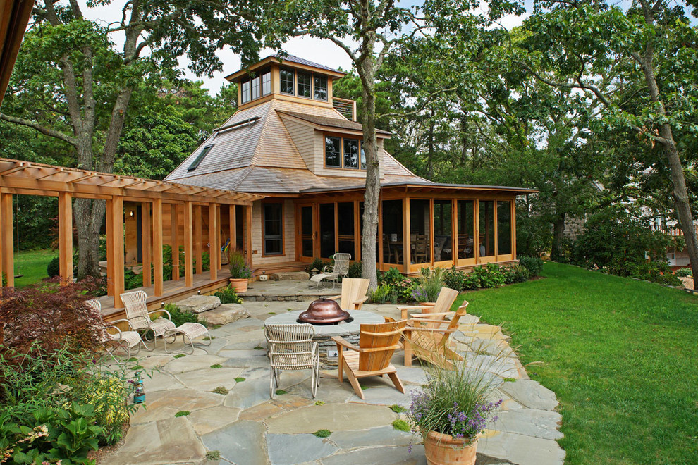 Cette image montre une grande terrasse arrière design avec un foyer extérieur, des pavés en pierre naturelle et une pergola.