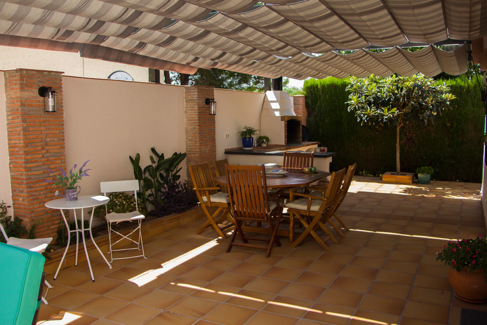 Foto de patio mediterráneo en patio trasero con jardín de macetas, suelo de baldosas y toldo