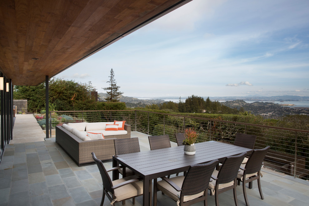 Aménagement d'une grande terrasse arrière moderne avec une cuisine d'été, des pavés en pierre naturelle et une extension de toiture.