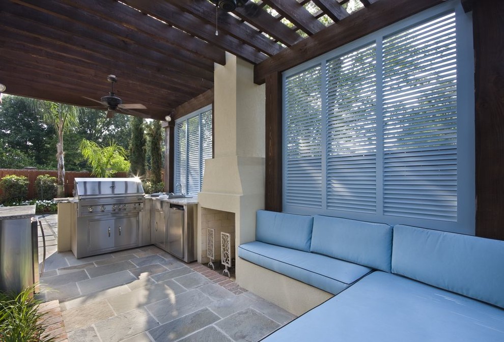 Aménagement d'une grande terrasse arrière avec une cuisine d'été, des pavés en pierre naturelle et une pergola.