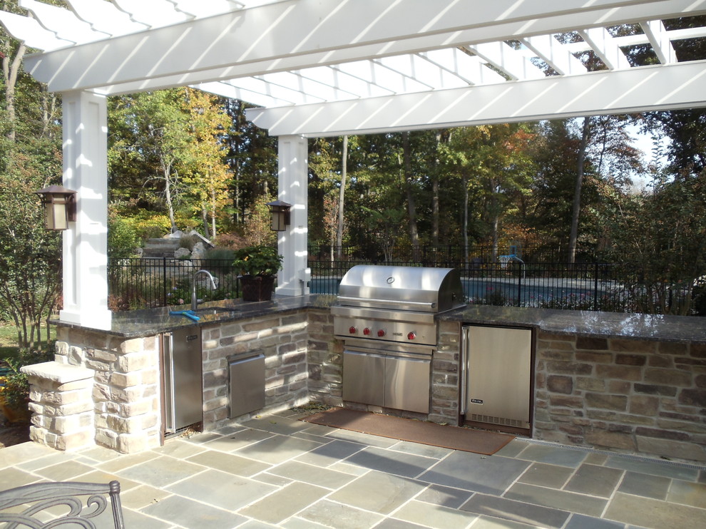 Example of a large classic backyard stone patio kitchen design in New York with a pergola