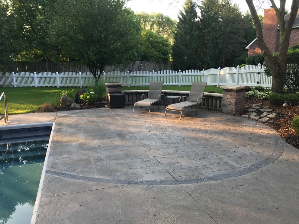Photo of a large classic back patio in Other with a fire feature, stamped concrete and a pergola.