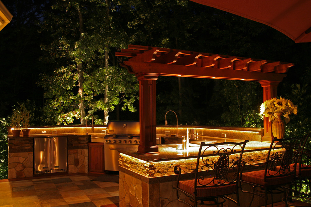 Large traditional back patio in New York with an outdoor kitchen, natural stone paving and a pergola.