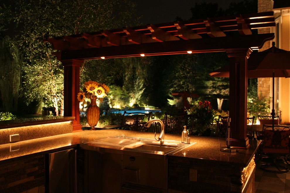 Cette image montre une grande terrasse arrière traditionnelle avec une cuisine d'été, des pavés en pierre naturelle et une pergola.