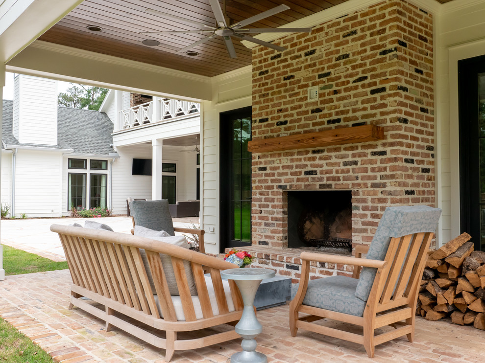 Medium sized farmhouse back patio in Houston with a fireplace, brick paving and an awning.