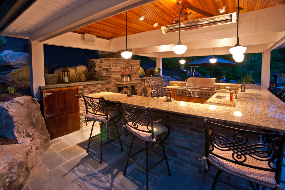 Exemple d'une grande terrasse arrière chic avec une cuisine d'été, des pavés en pierre naturelle et une extension de toiture.