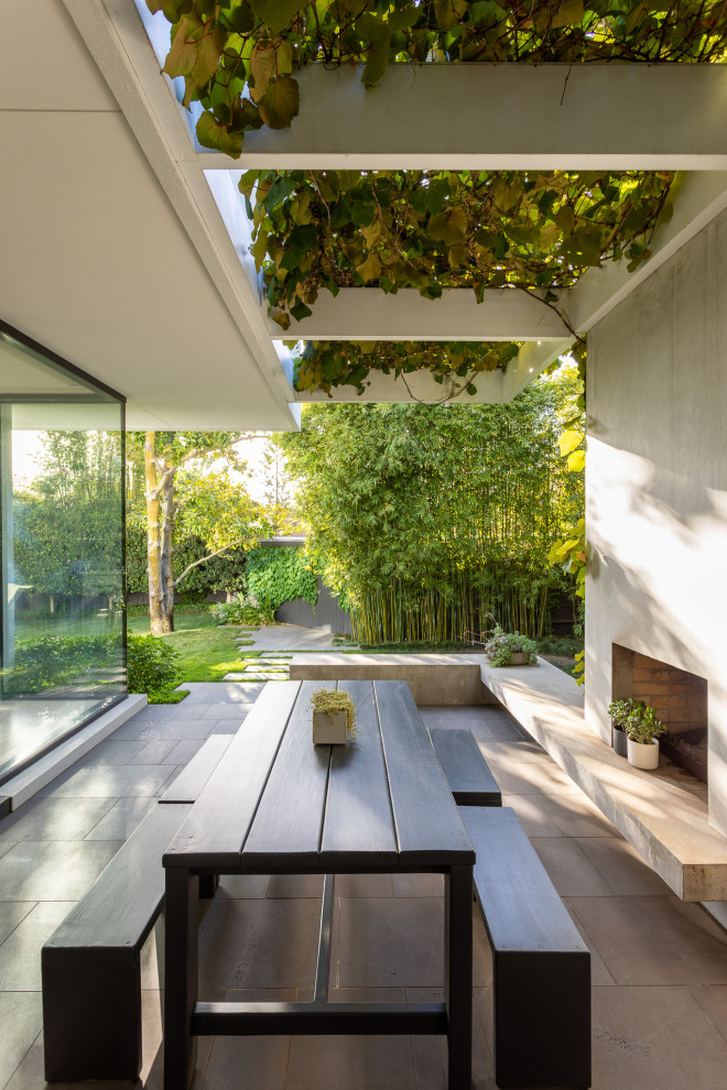Foto di un patio o portico minimal di medie dimensioni e dietro casa con un caminetto, pavimentazioni in pietra naturale e una pergola