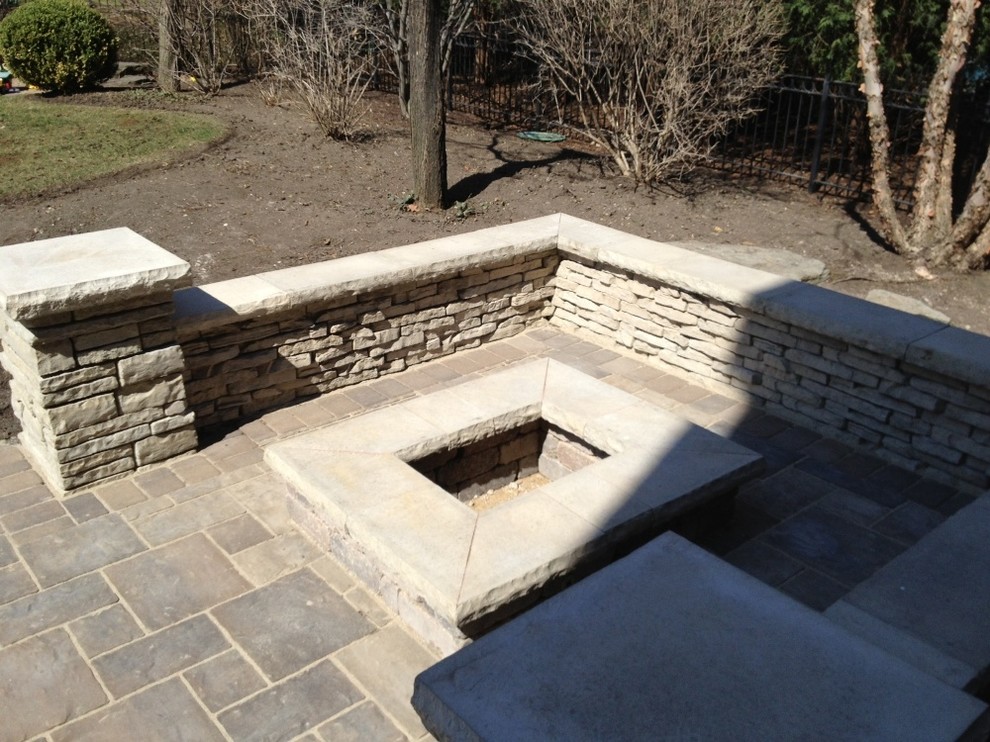 This is an example of a large traditional back patio in Chicago with a fire feature, natural stone paving and no cover.