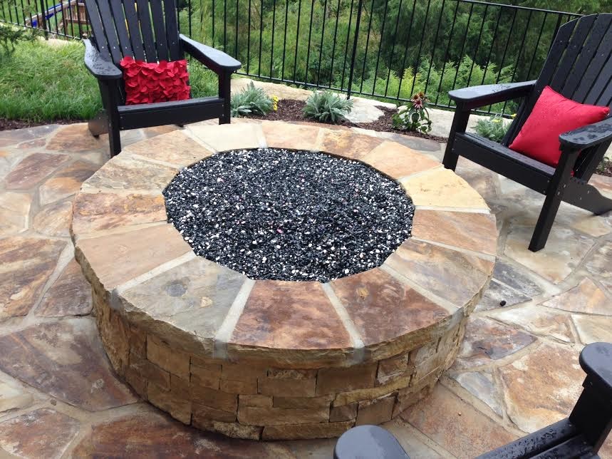 This is an example of a medium sized traditional back patio in Kansas City with a fire feature and natural stone paving.