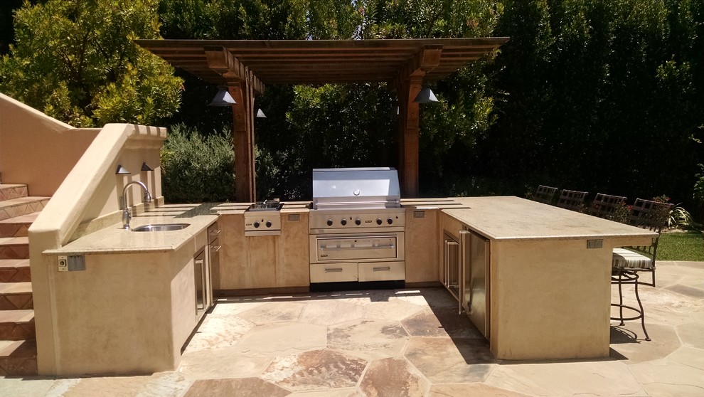 Cette image montre une terrasse arrière méditerranéenne avec une cuisine d'été, des pavés en pierre naturelle et une pergola.