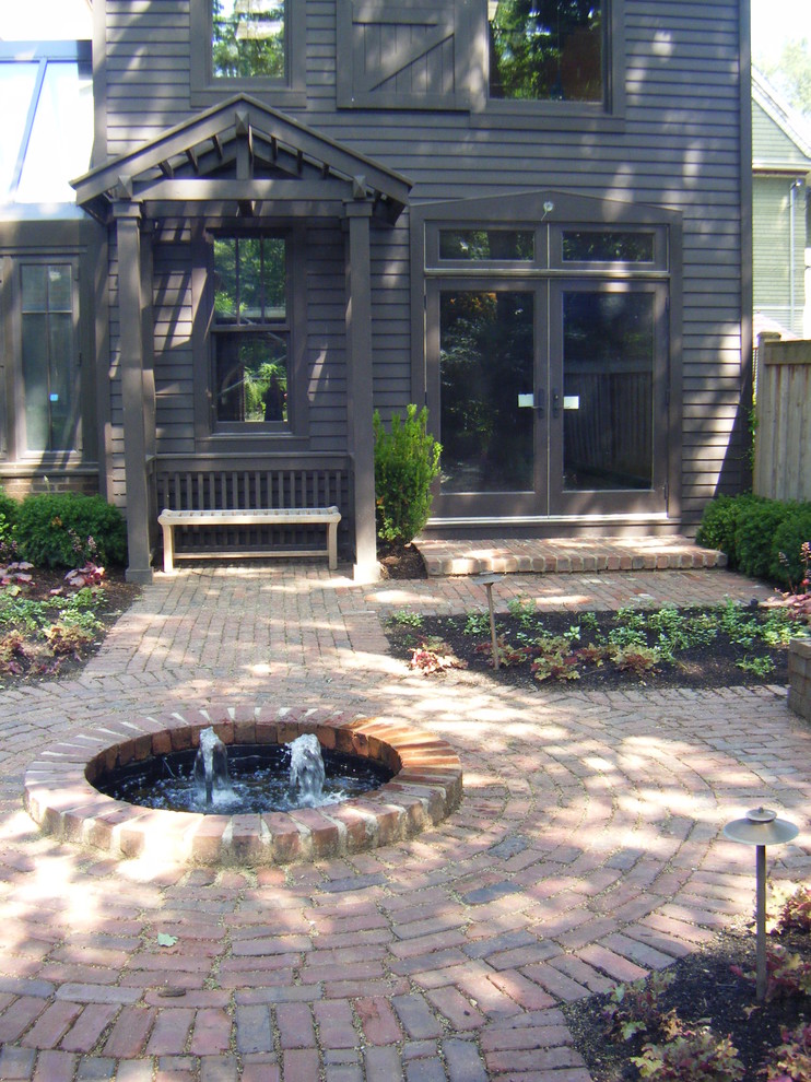 Ejemplo de patio clásico de tamaño medio sin cubierta en patio trasero con fuente y adoquines de ladrillo