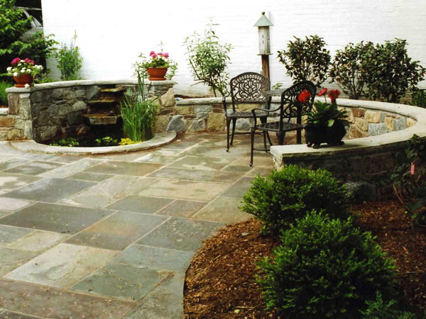 Ejemplo de patio ecléctico de tamaño medio sin cubierta en patio trasero con fuente y adoquines de piedra natural