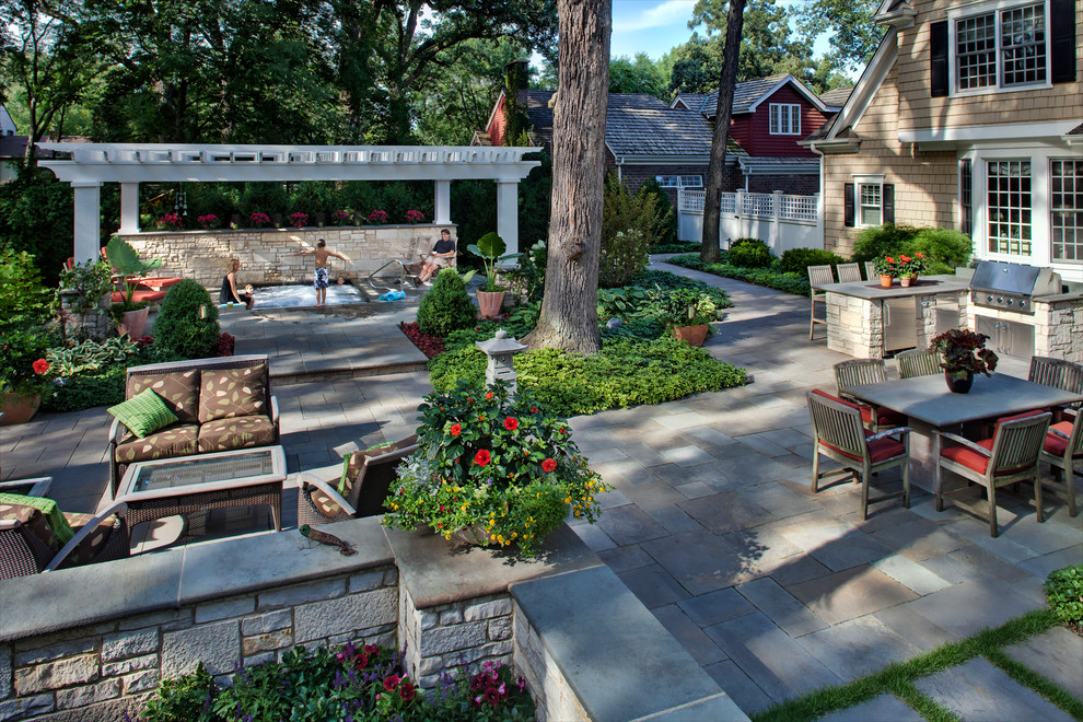 Exemple d'une grande terrasse arrière chic avec une cuisine d'été, des pavés en pierre naturelle et une pergola.