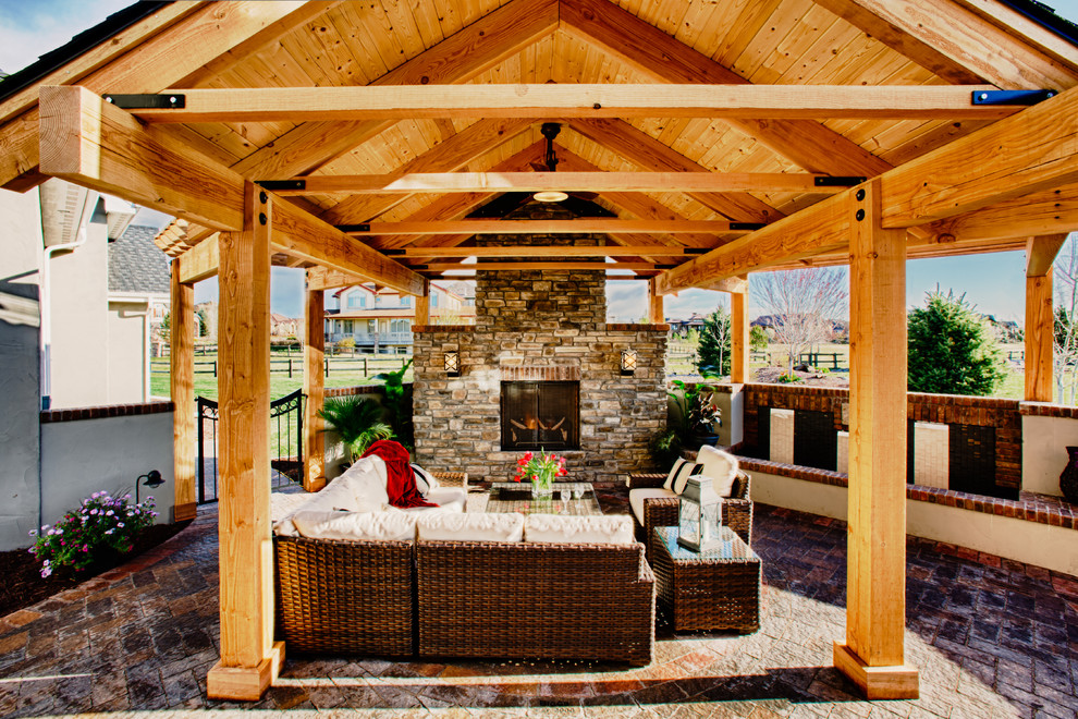 Aménagement d'une grande terrasse arrière classique avec un foyer extérieur, des pavés en béton et une extension de toiture.