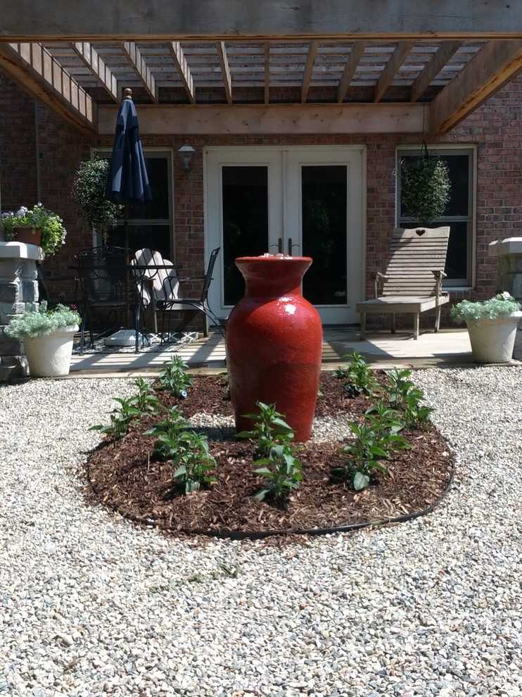 This is an example of a medium sized modern back patio in Detroit with a water feature, gravel and a pergola.