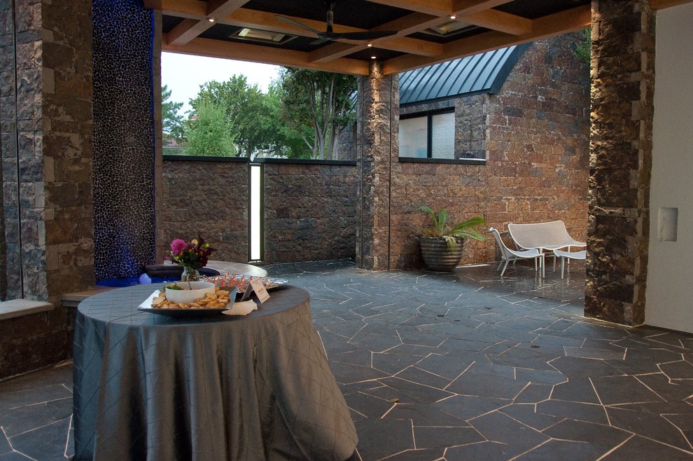 Cette image montre une grande terrasse latérale design avec un point d'eau, des pavés en pierre naturelle et une extension de toiture.