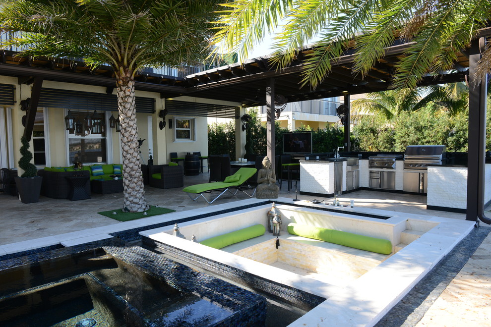 Réalisation d'une très grande terrasse arrière design avec une cuisine d'été, des pavés en pierre naturelle et une pergola.