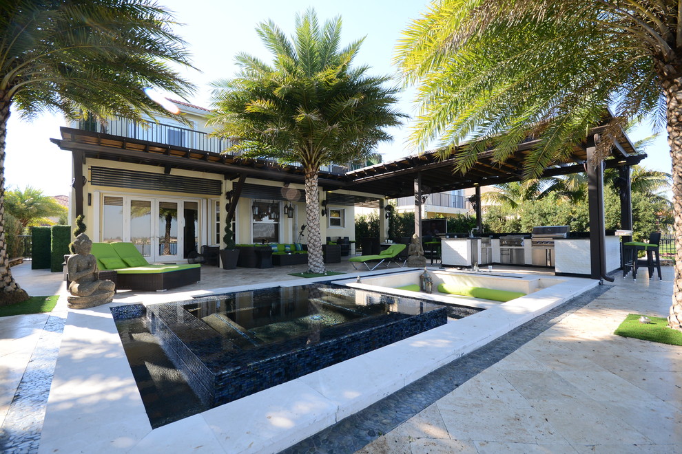 Expansive contemporary back patio in Miami with an outdoor kitchen, natural stone paving and a pergola.