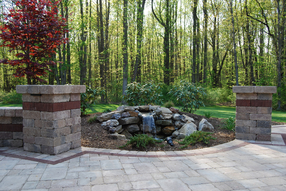 Modelo de patio clásico renovado de tamaño medio sin cubierta en patio trasero con fuente y adoquines de ladrillo