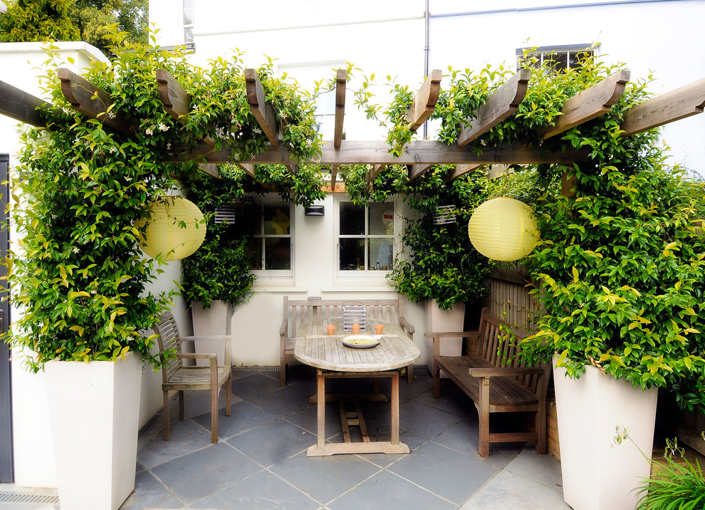 Example of a small tuscan backyard stone patio design in London with a pergola