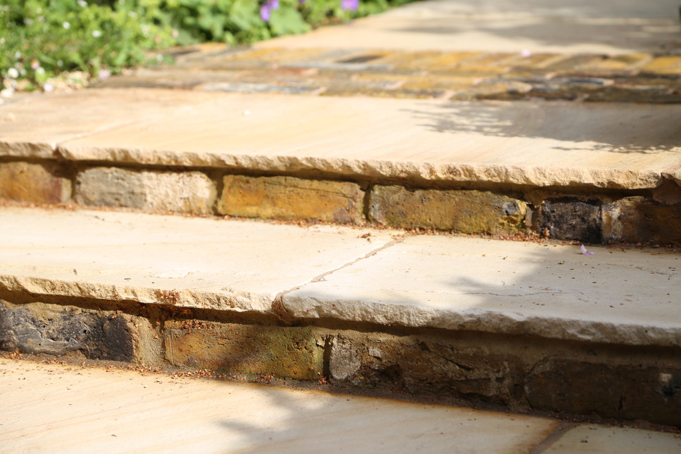 This is an example of a small rustic back patio in London with natural stone paving.