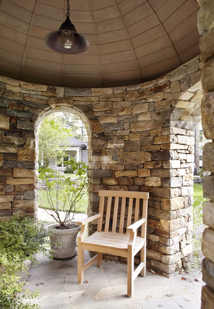 Immagine di un patio o portico tradizionale dietro casa con pavimentazioni in pietra naturale e un gazebo o capanno