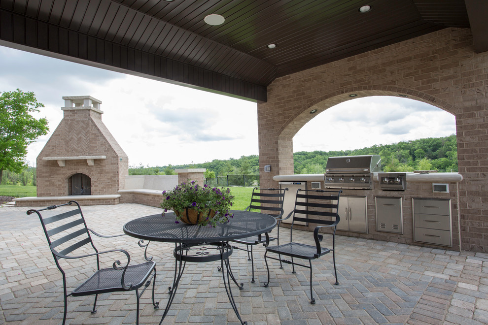 Large elegant backyard brick patio kitchen photo in Other with an awning
