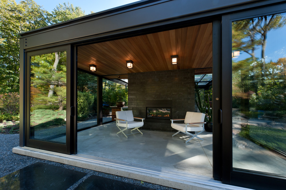 Ispirazione per un piccolo patio o portico moderno dietro casa con un focolare, lastre di cemento e un tetto a sbalzo
