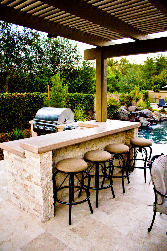Large classic back patio in Sacramento with an outdoor kitchen, natural stone paving and a pergola.