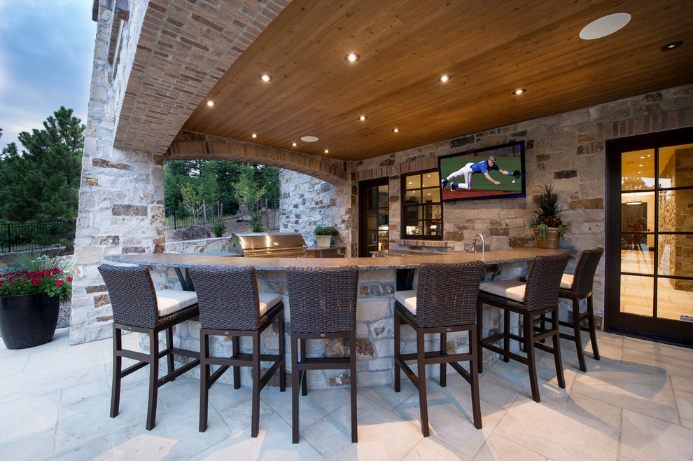 This is an example of an expansive rustic back patio in Denver with an outdoor kitchen, natural stone paving and a pergola.