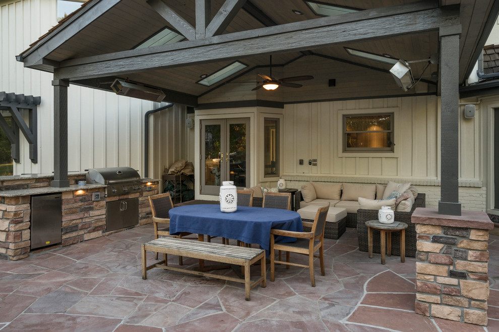 This is an example of a large classic back patio in Denver with an outdoor kitchen, natural stone paving and a roof extension.