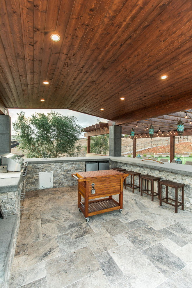 Aménagement d'une grande terrasse arrière contemporaine avec une cuisine d'été, des pavés en pierre naturelle et une pergola.