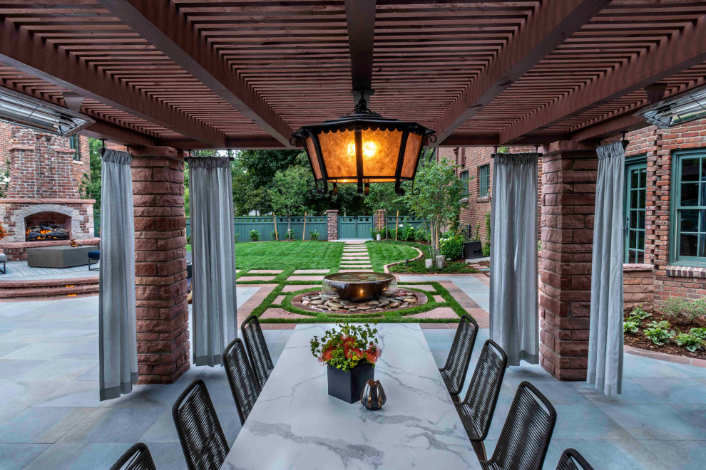 This is an example of an expansive traditional back patio in Denver with an outdoor kitchen, natural stone paving and a pergola.