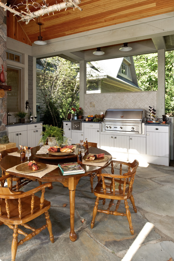 Large elegant backyard stone patio kitchen photo in Other with a roof extension
