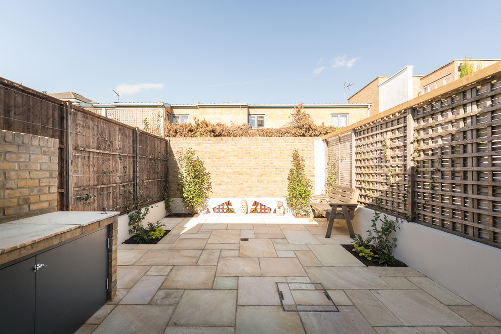 This is an example of a small contemporary back patio in London with an outdoor kitchen and natural stone paving.
