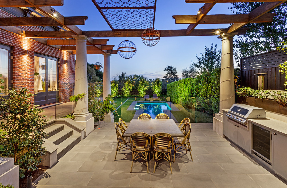 Cette image montre une grande terrasse traditionnelle avec une cuisine d'été, du carrelage et une pergola.