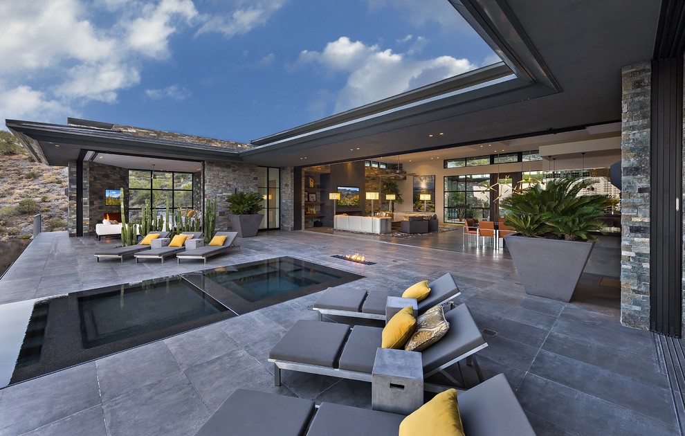 Inspiration pour une très grande terrasse arrière minimaliste avec un foyer extérieur, des pavés en pierre naturelle et une extension de toiture.