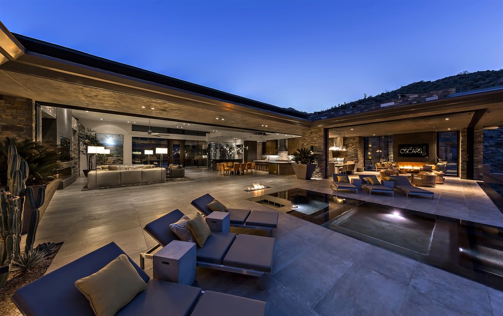 Réalisation d'une très grande terrasse arrière minimaliste avec des pavés en pierre naturelle et une extension de toiture.