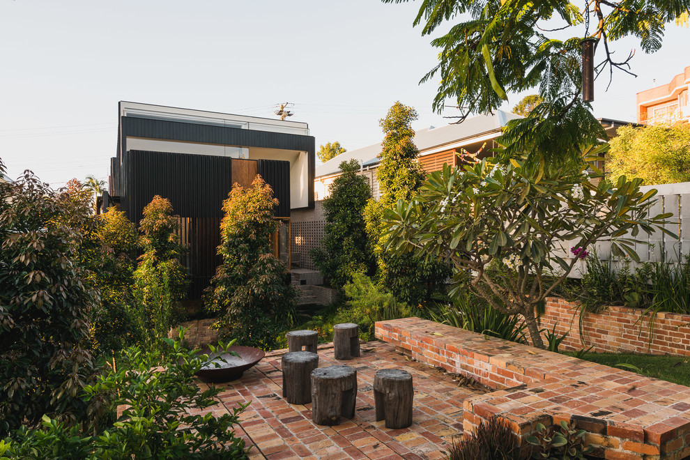 Moderner Patio hinter dem Haus mit Pflastersteinen und Feuerstelle in Brisbane