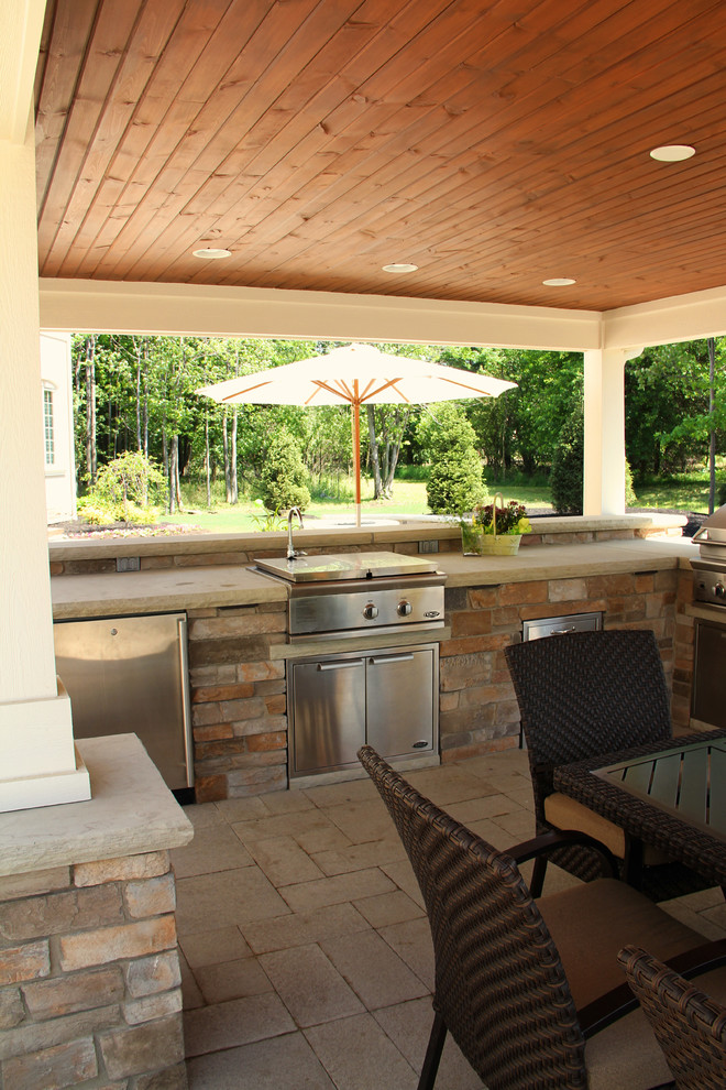 Modelo de patio clásico grande en patio trasero con cocina exterior, adoquines de hormigón y cenador
