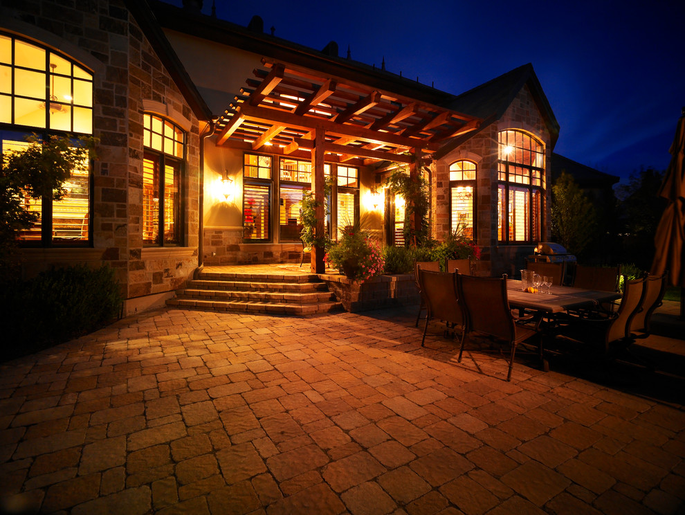 Modelo de patio clásico grande en patio trasero con adoquines de hormigón y pérgola