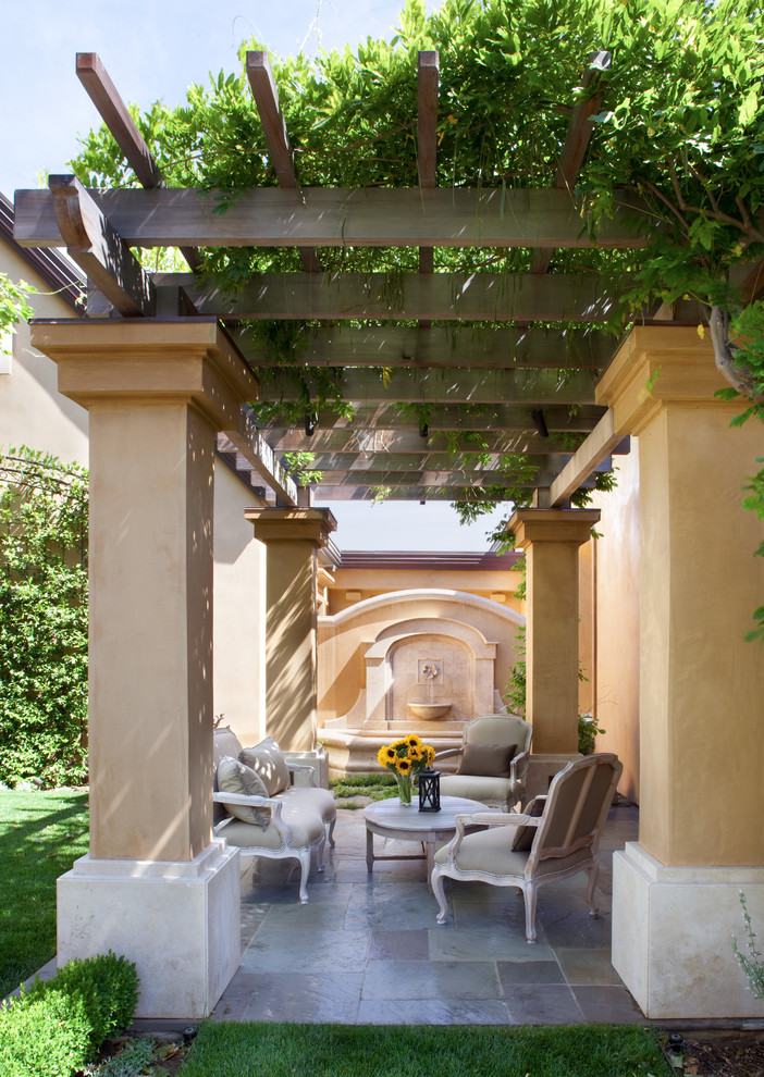 Imagen de patio mediterráneo pequeño en patio trasero con fuente, adoquines de piedra natural y pérgola